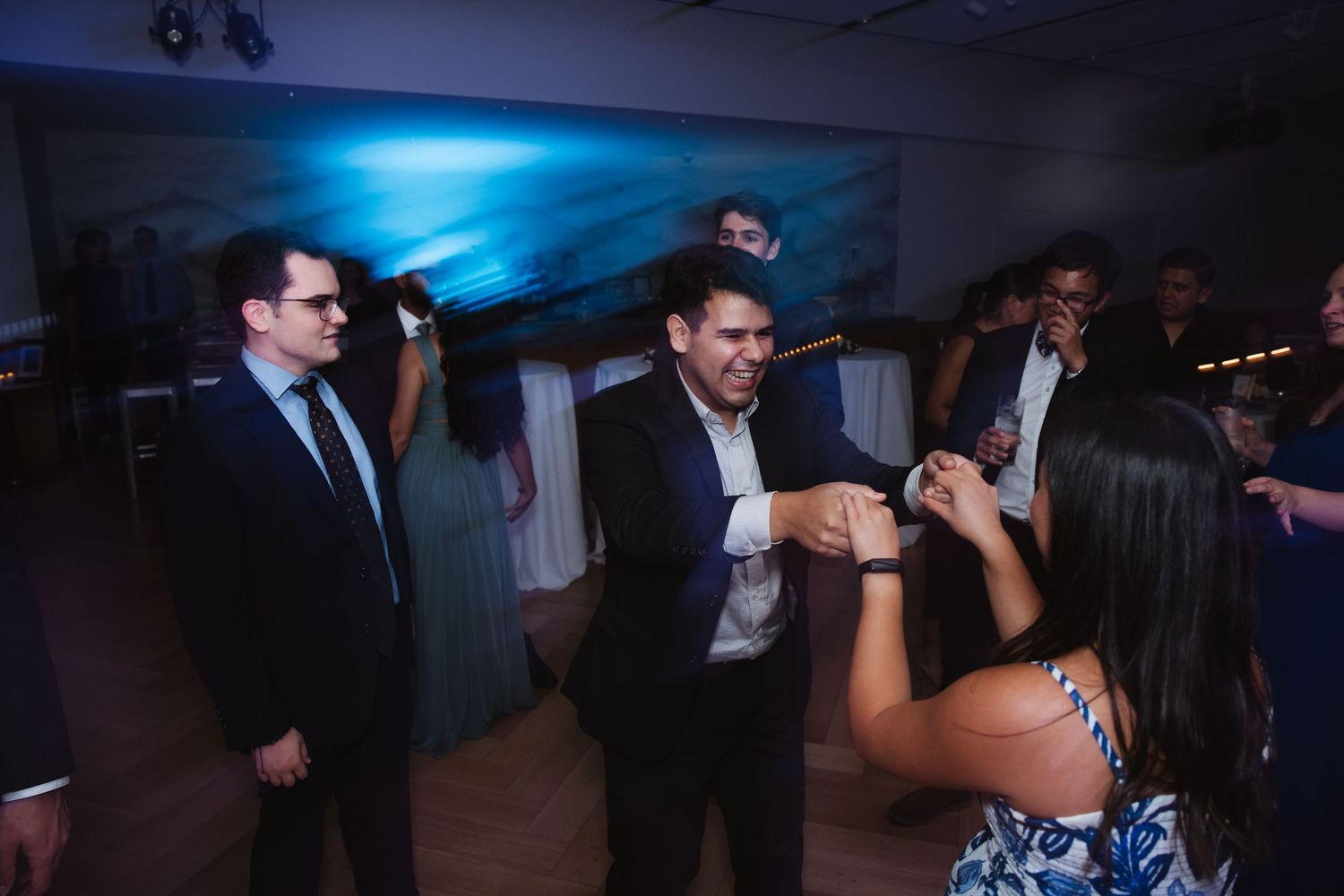 Wedding guests dancing and socializing at evening reception with blue ambient lighting.