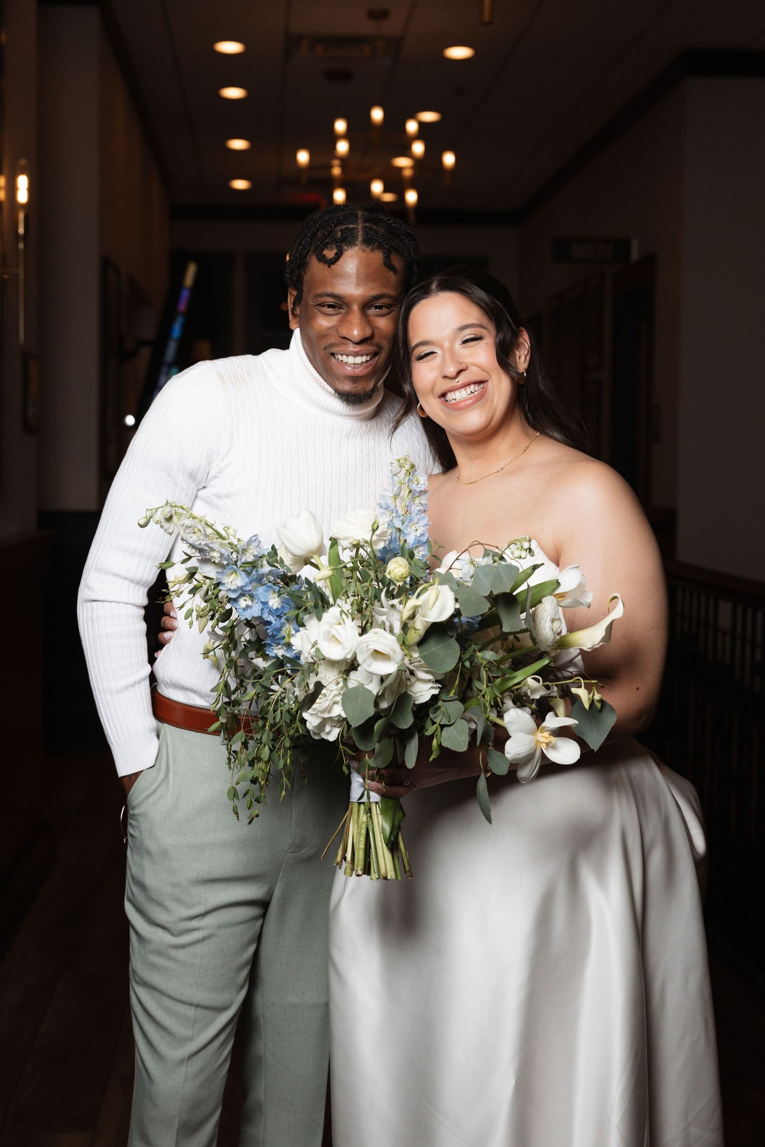 Smiling bride and groom holding large blue and white floral bouquets in elegant indoor venue.