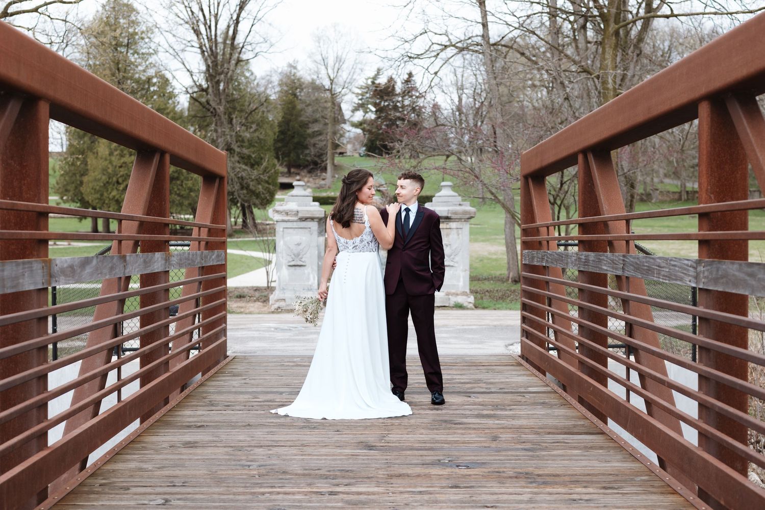A bride and groom share a romantic moment on a wooden bridge surrounded by lush greenery on their wedding day.
