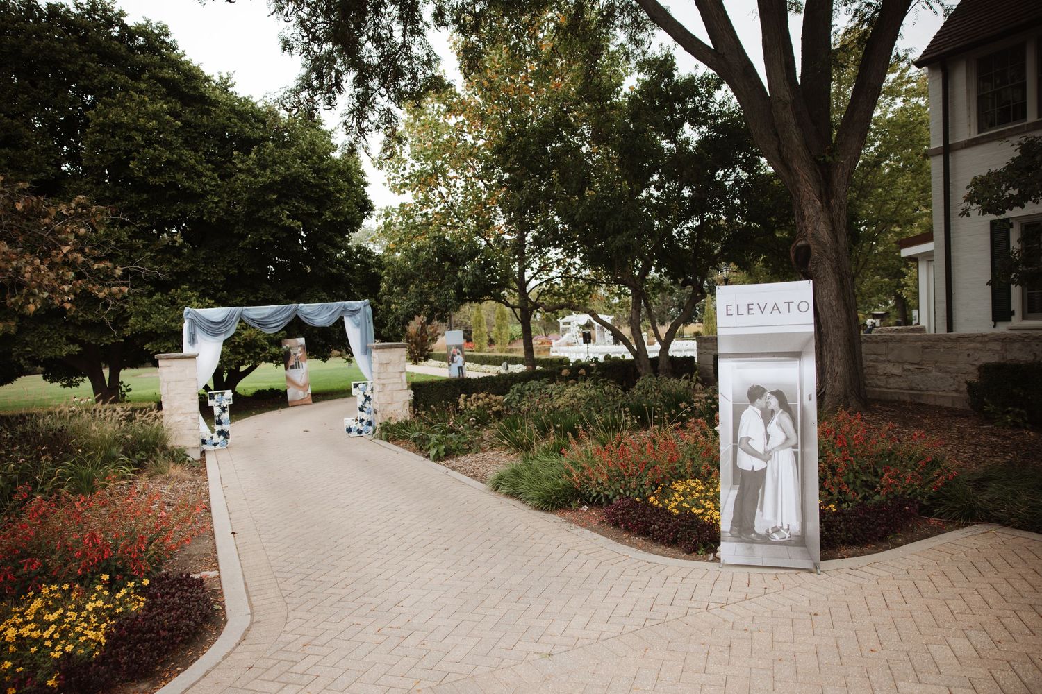Elegant wedding venue entrance with floral arch, brick pathway, and event signage.
