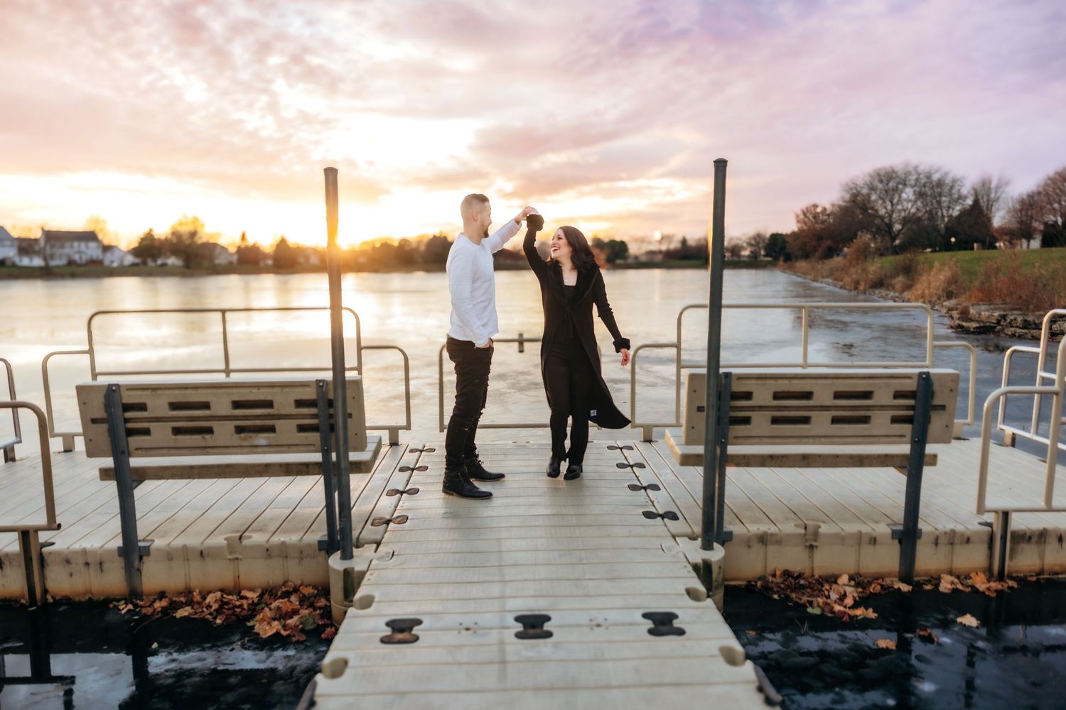 Couple dancing joyfully on a dock at sunset with a scenic lake in the background.