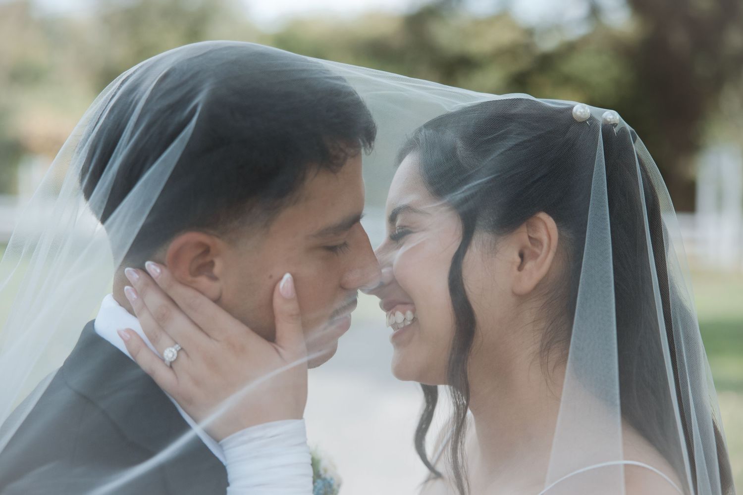 Bride and groom share an intimate moment under a flowing wedding veil, smiling at each other on their wedding day.