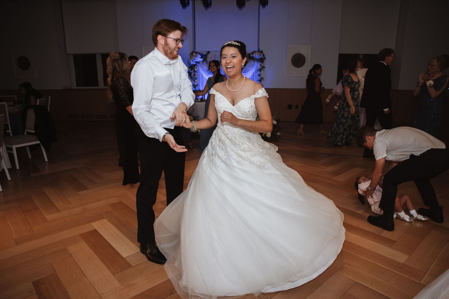 Bride in white ball gown dancing with groom in white shirt on wooden dance floor at wedding reception.