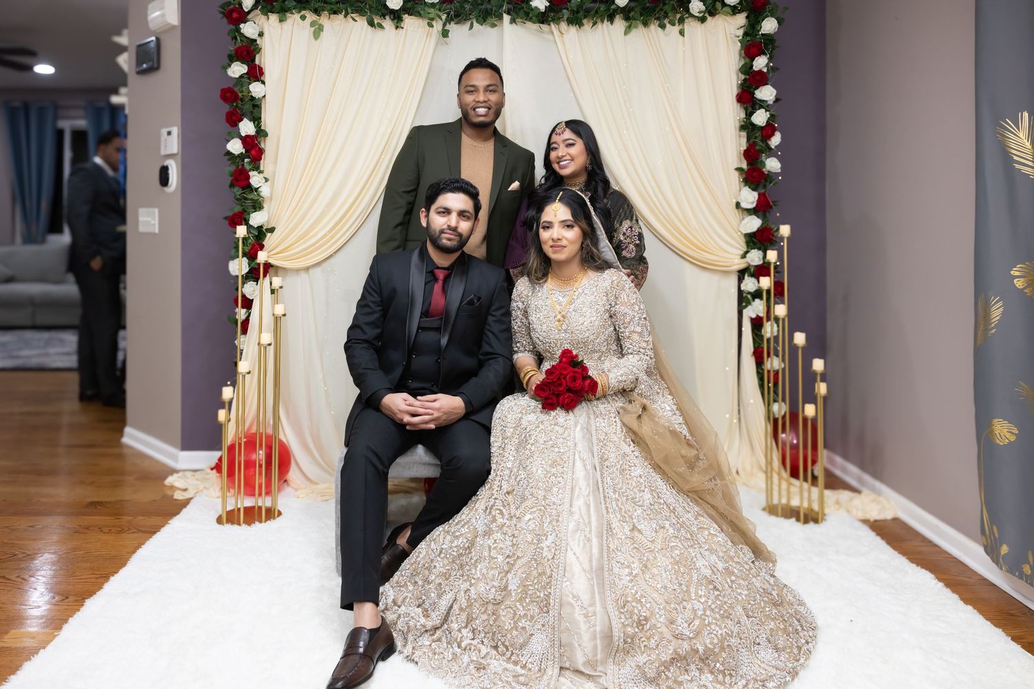 South Asian bride and groom with two friends posing at decorated wedding mandap backdrop.