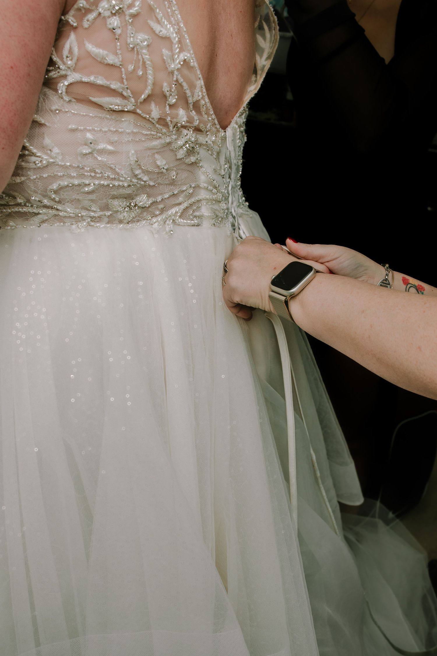 Close-up of hands tying the back of an intricate beaded white wedding dress.