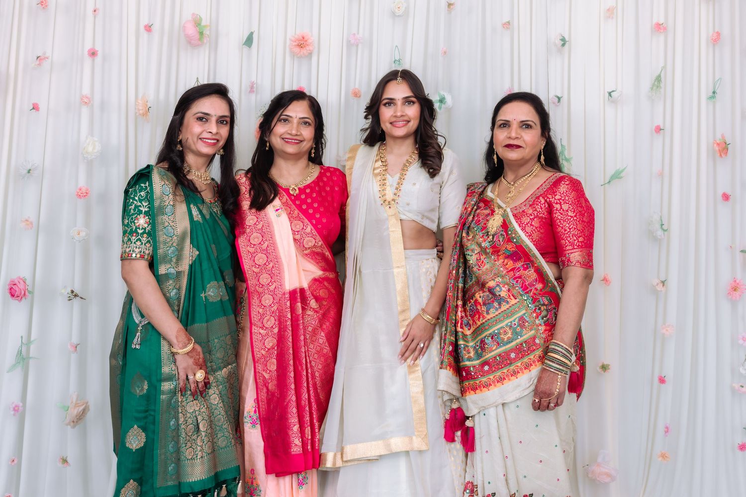 Four women in colorful traditional Indian attire including green, pink, white, and printed sarees at a celebration.
