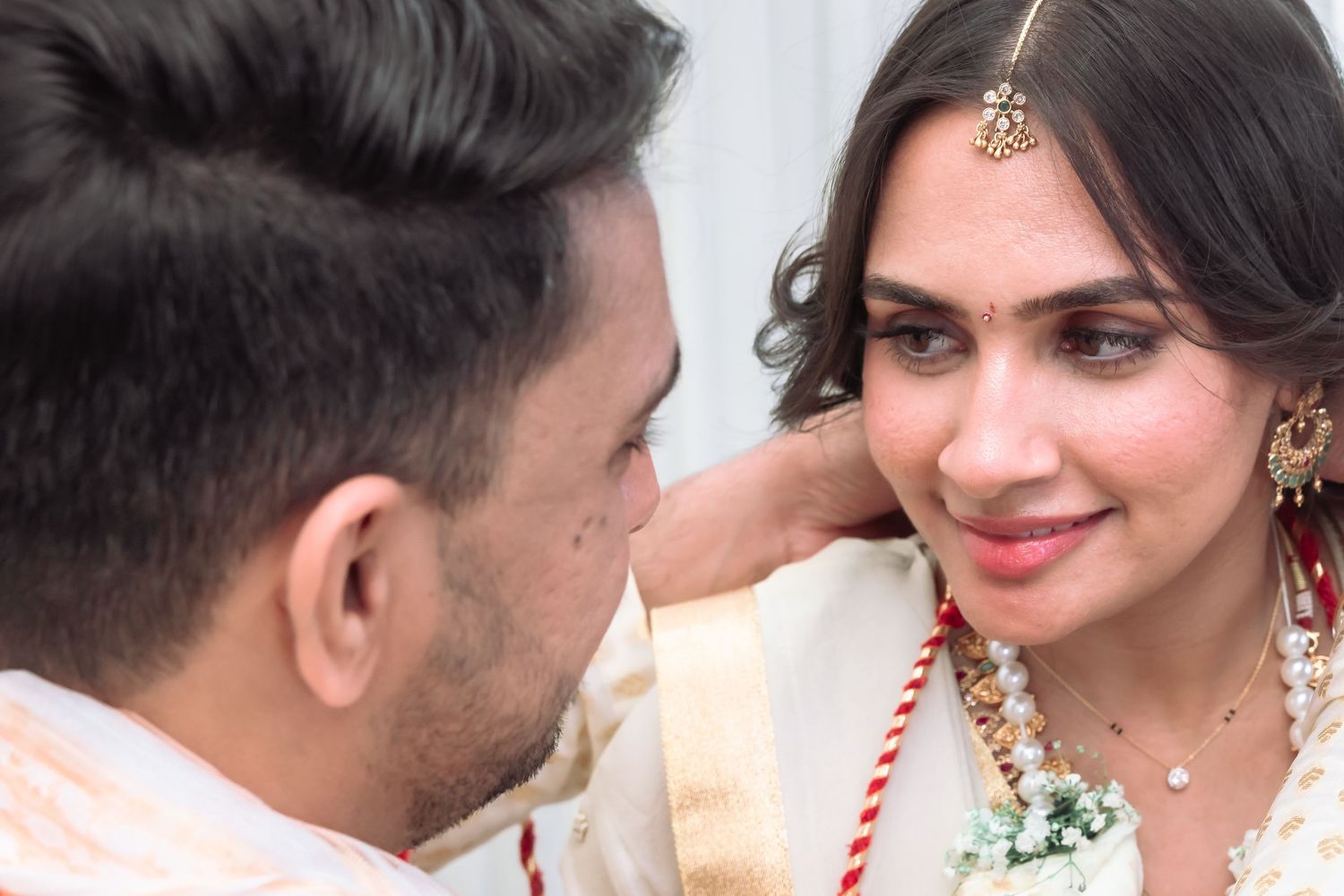 Close-up portrait of radiant Indian bride with maang tikka and groom during wedding ceremony.
