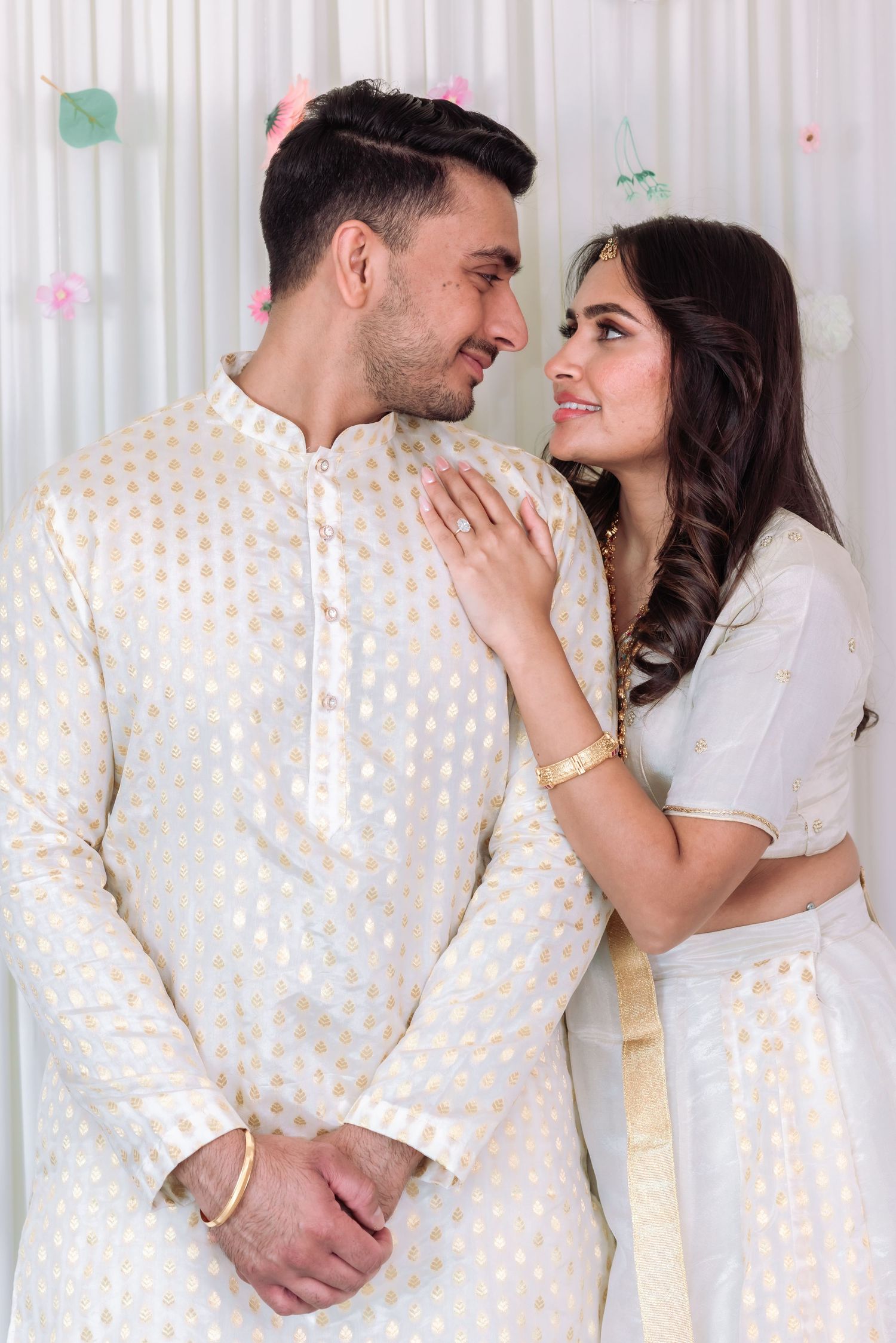 Indian couple in matching white and gold traditional outfits sharing a romantic gaze together.