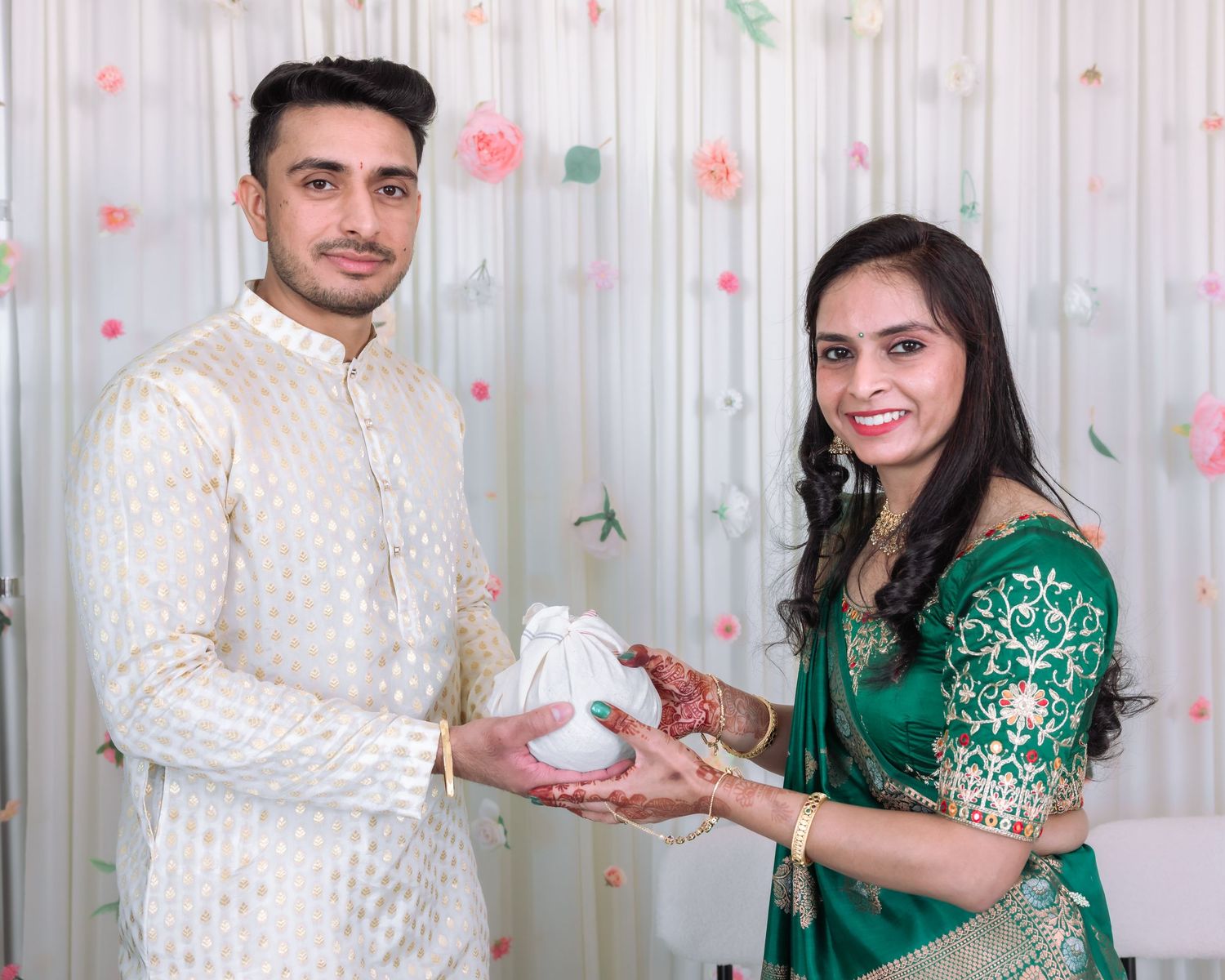 South Asian couple in traditional Indian attire holding white gift bag at festive event.