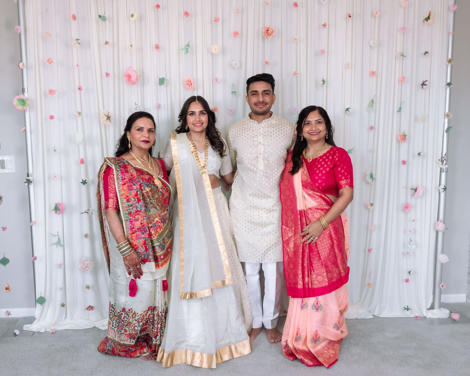 Indian family of four posing with bride and groom in traditional white and pink wedding attire.