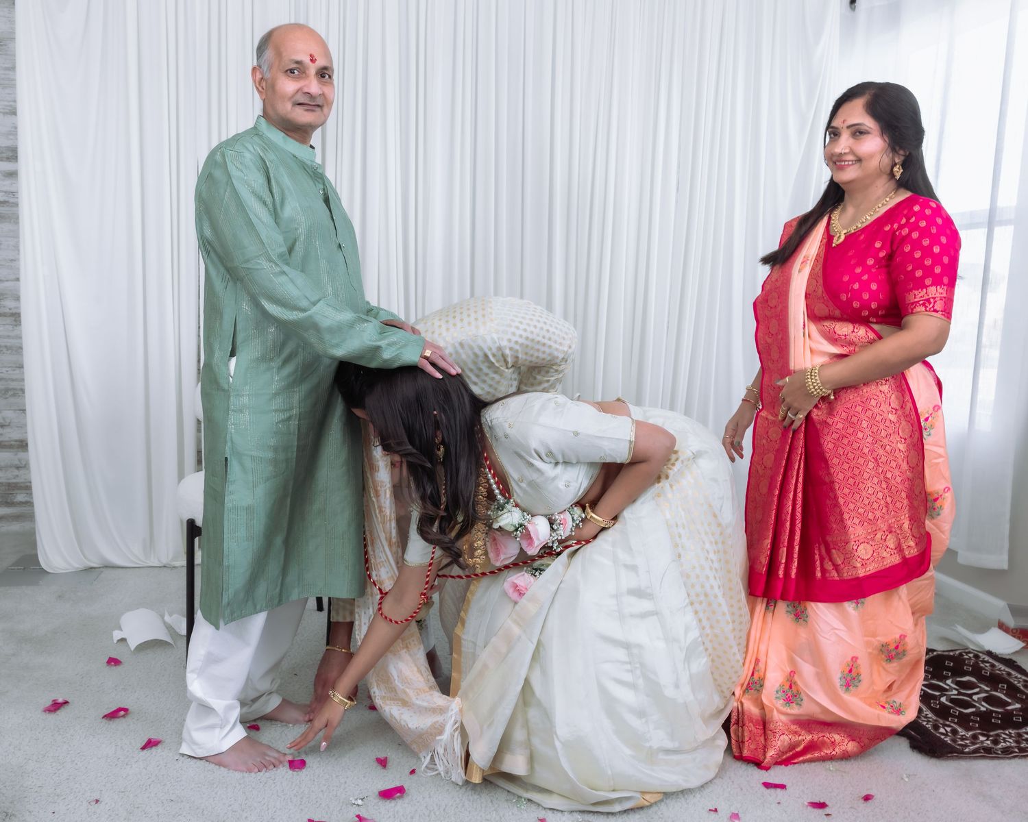 Indian bride in white lehenga touching elder's feet in traditional blessing ritual at Hindu wedding.
