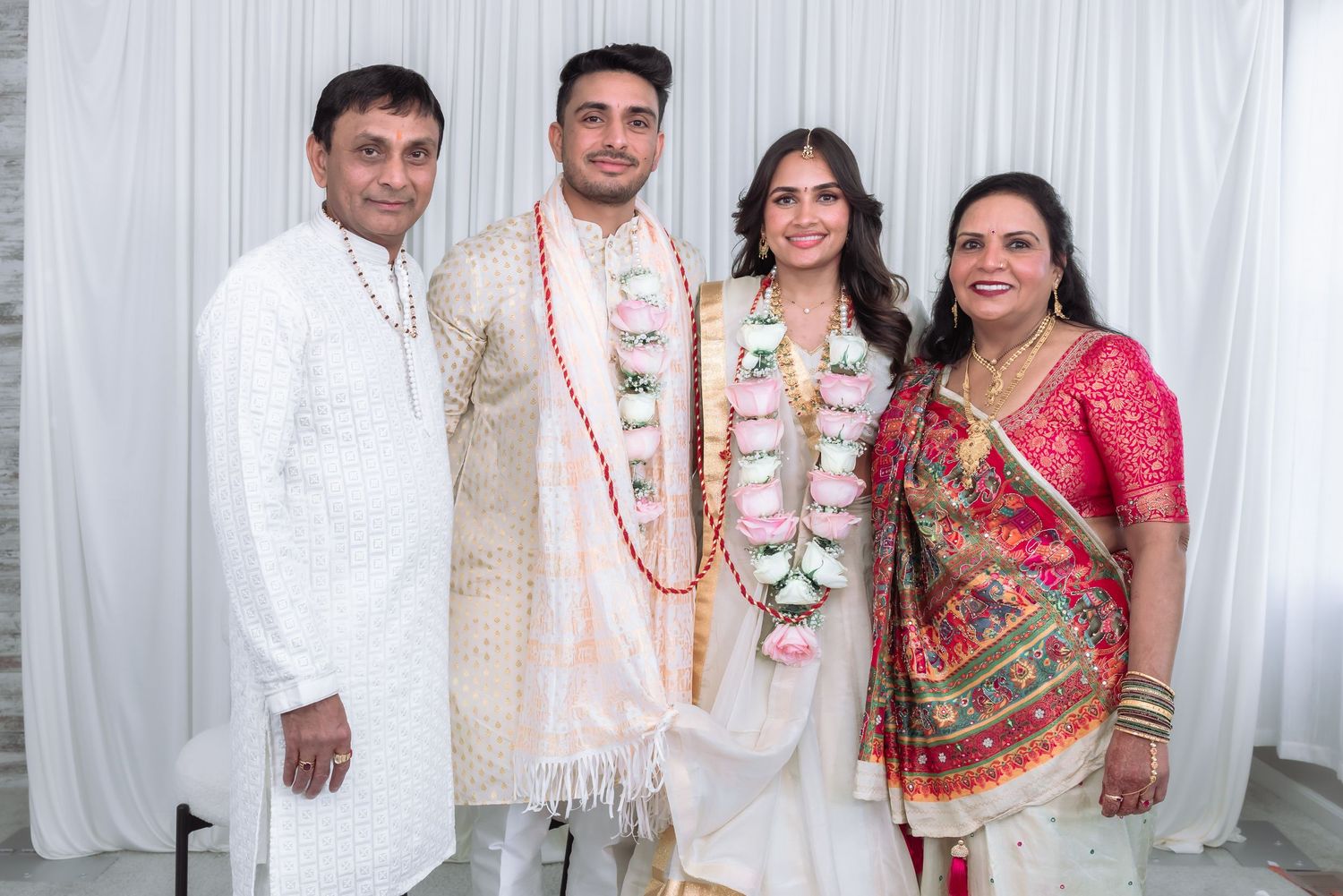 Indian newlyweds wearing floral garlands pose with parents in traditional wedding attire.
