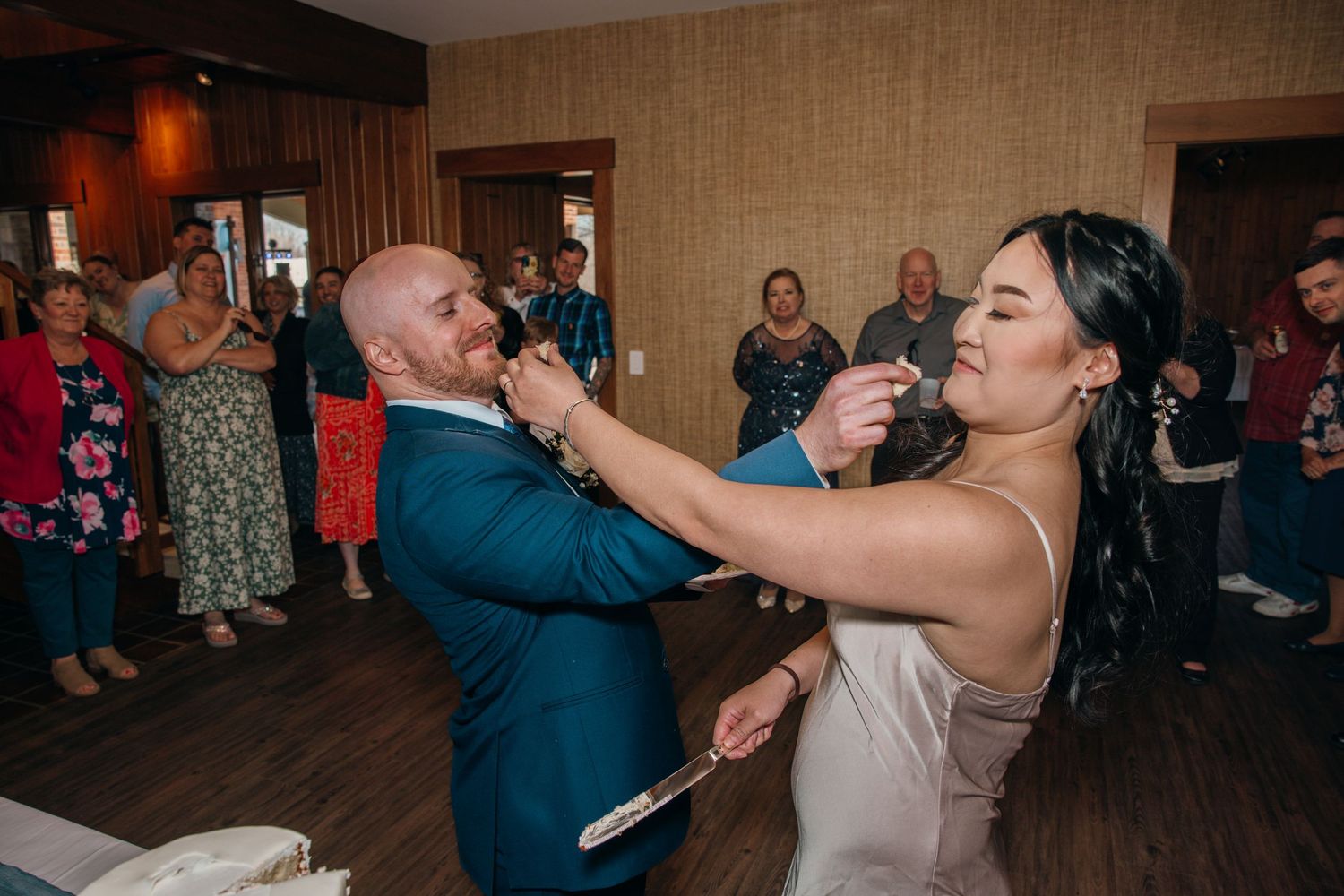 Bride and groom playfully feeding each other wedding cake during their reception celebration.