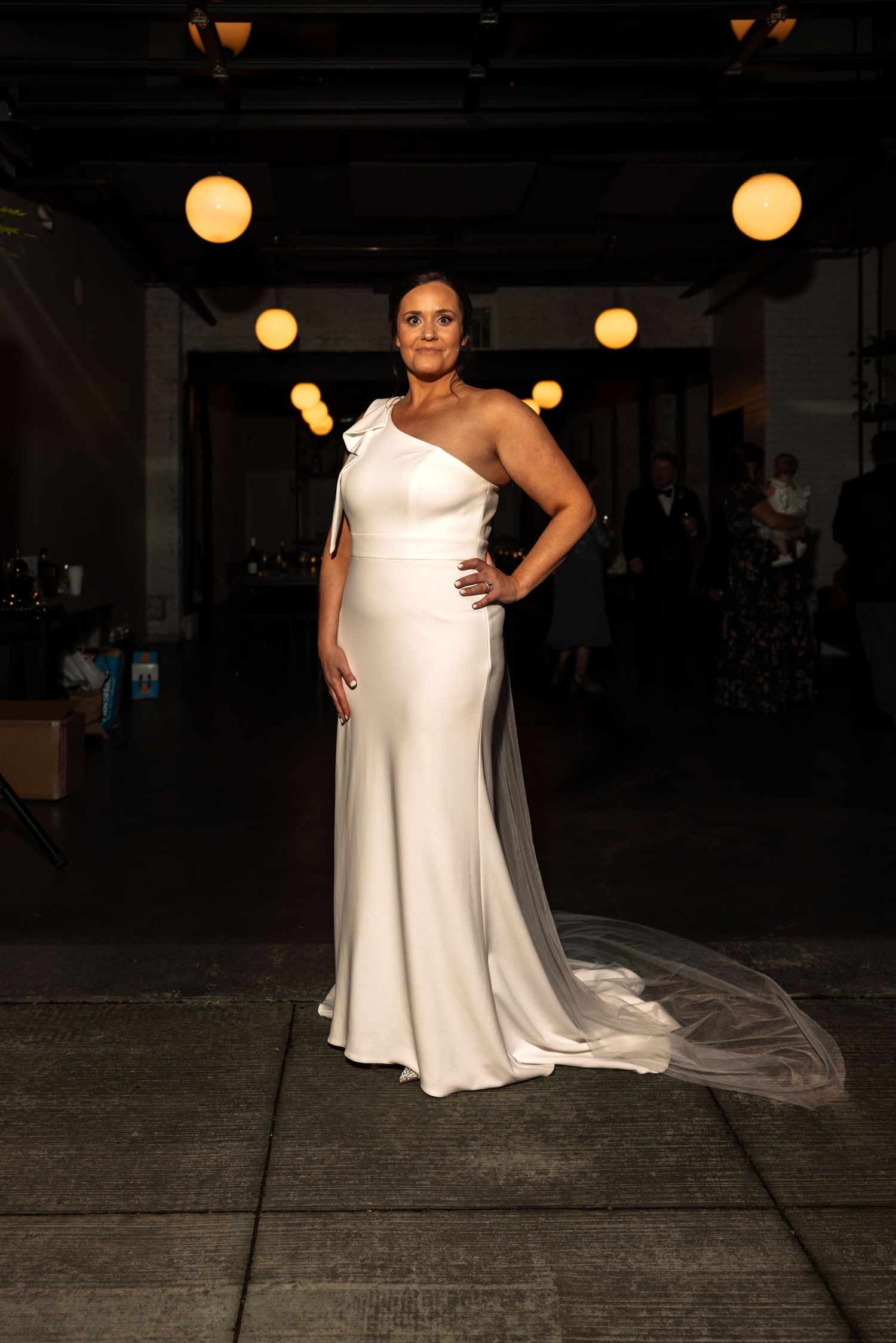 Bride posing confidently in a sleek one-shoulder white gown with long veil.