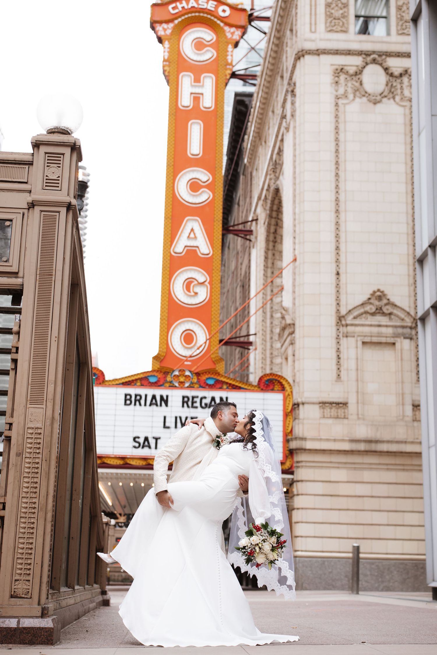 Groom lifts bride in white dress beneath the iconic Chicago Theatre neon sign downtown.