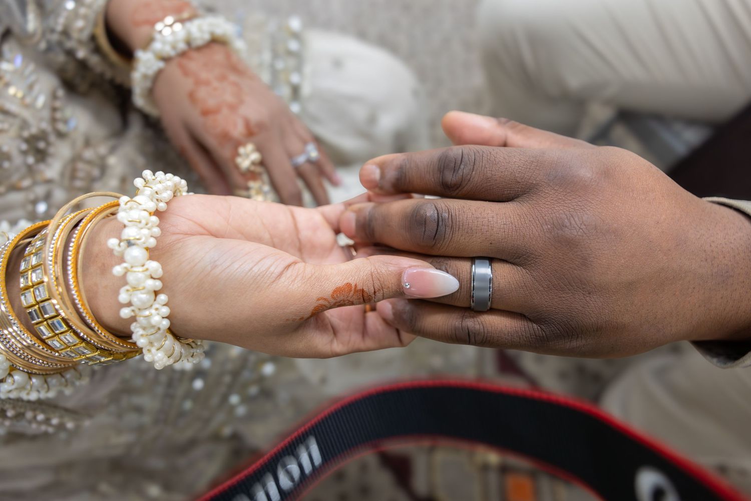 Bride's hand adorned with gold bangles and henna held by groom wearing a silver wedding band.