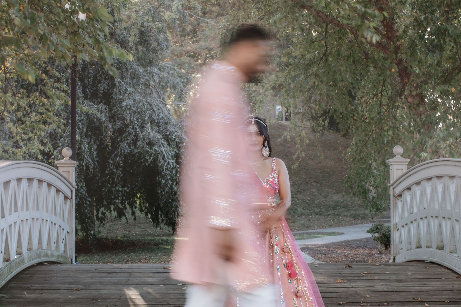 Motion blur artistic shot of Indian couple in pink wedding outfits near garden bridge.