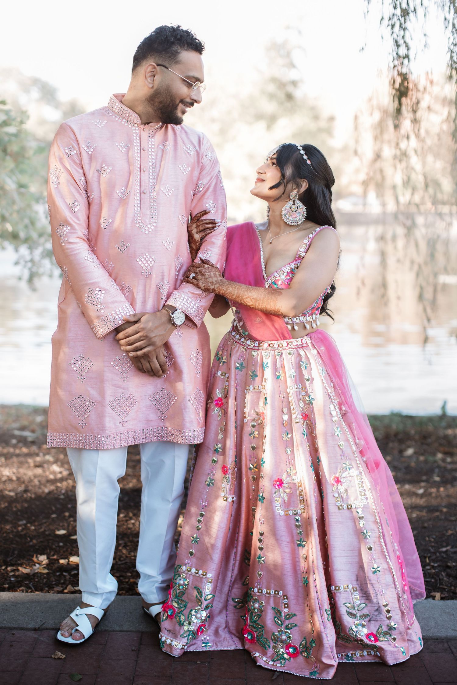 Couple in matching pink Indian wedding outfits sharing a joyful moment outdoors.