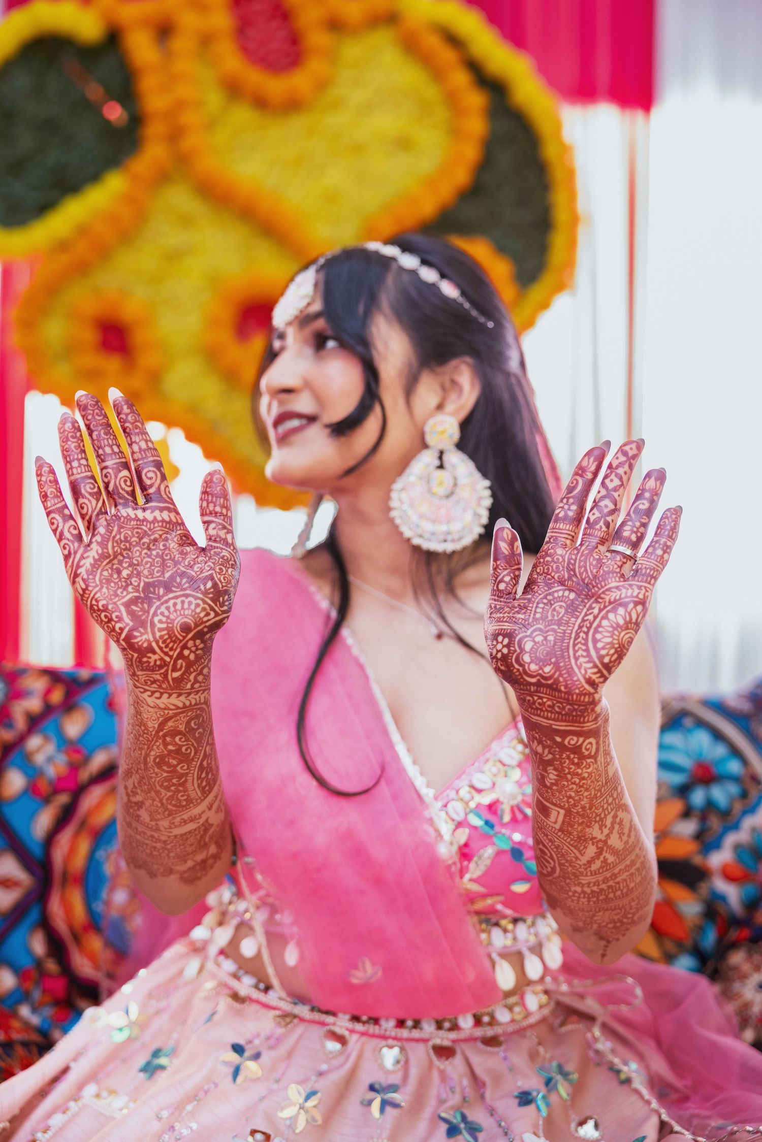 Indian bride in pink lehenga proudly displaying elaborate bridal mehndi henna on both hands.