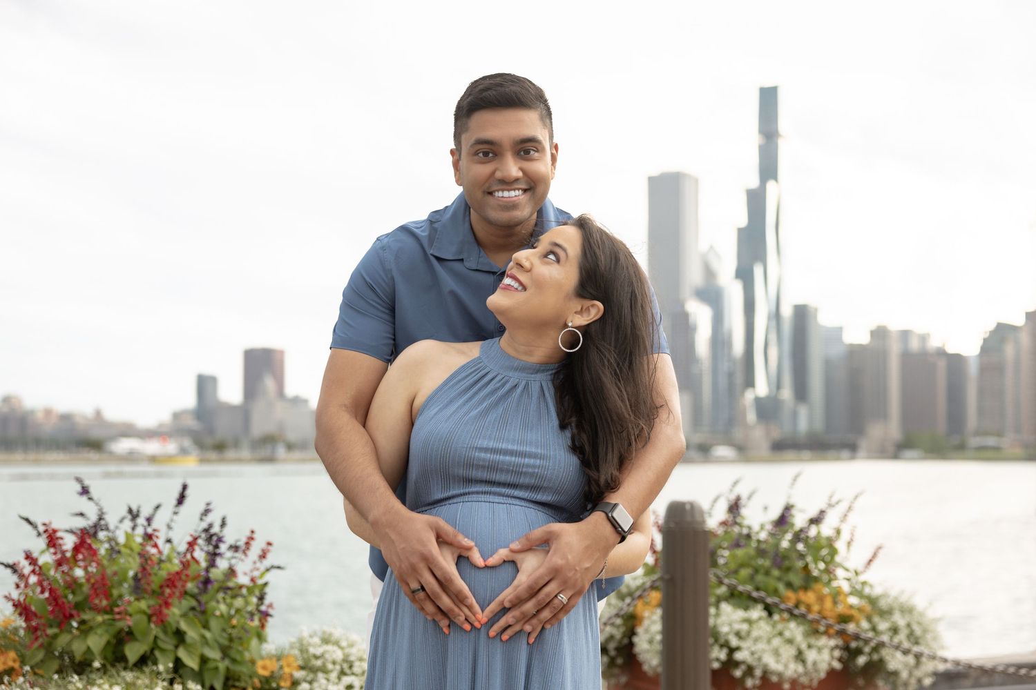 Happy expectant couple making heart shape on pregnant belly with Chicago city skyline behind them.
