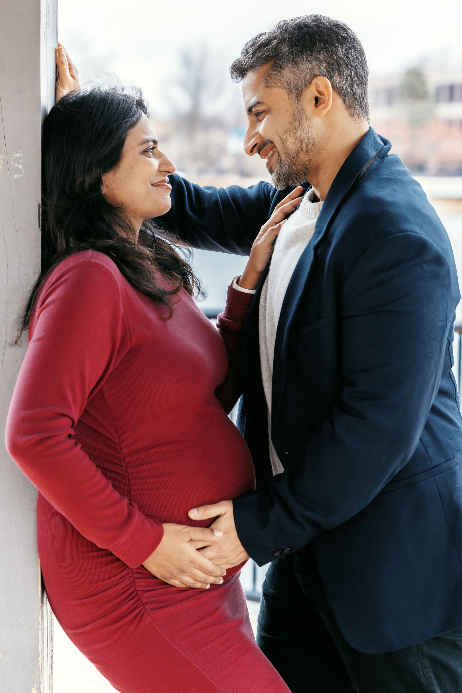 Smiling expecting couple gazing at each other affectionately near a wall.