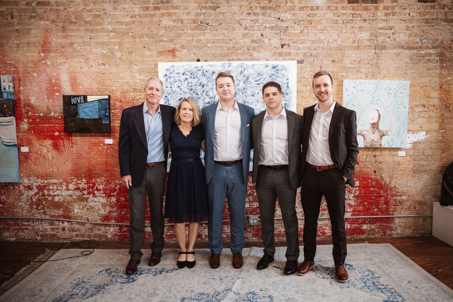 Five smiling professionals pose together at an art gallery event with abstract paintings on display.