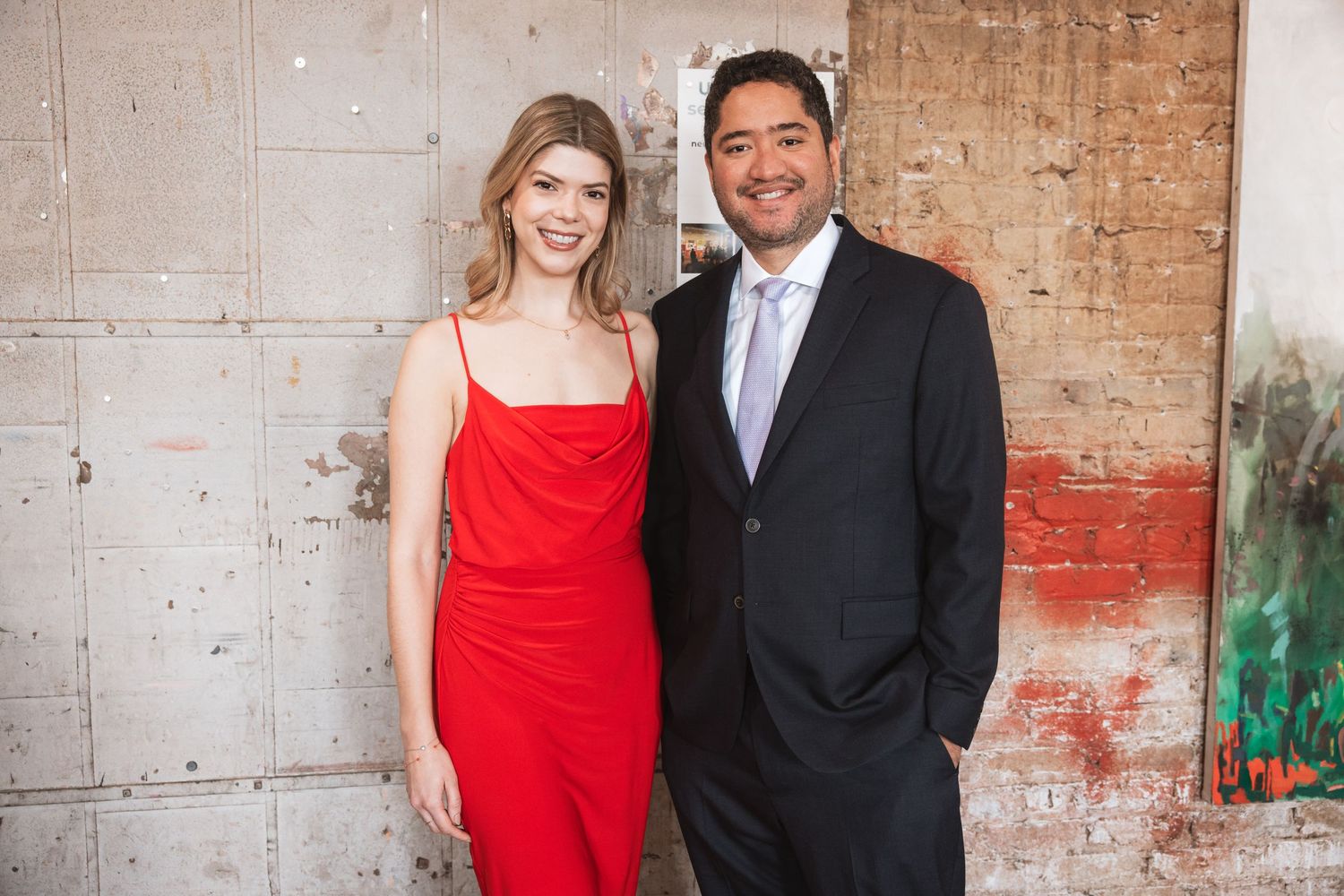 Couple posing together, woman in red dress and man in dark suit, at a formal event.