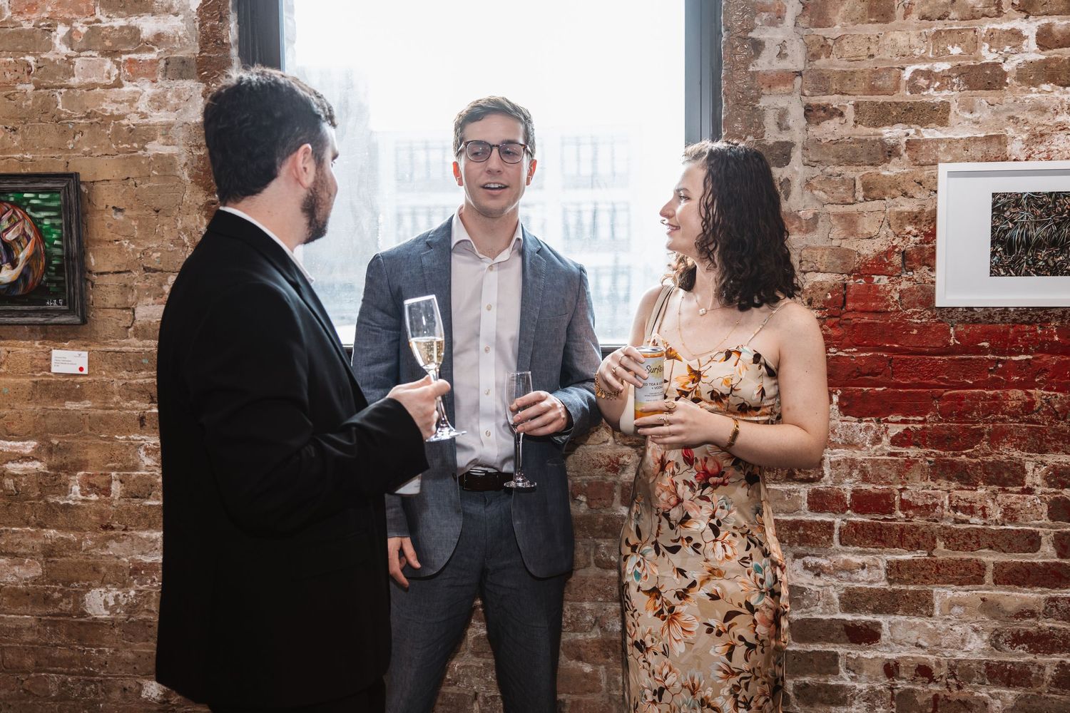 Three guests in formal attire enjoying champagne and conversation at an upscale brick-wall venue.