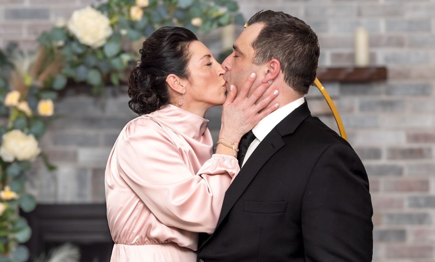 Couple sharing a romantic first kiss at their wedding ceremony with floral arch backdrop.