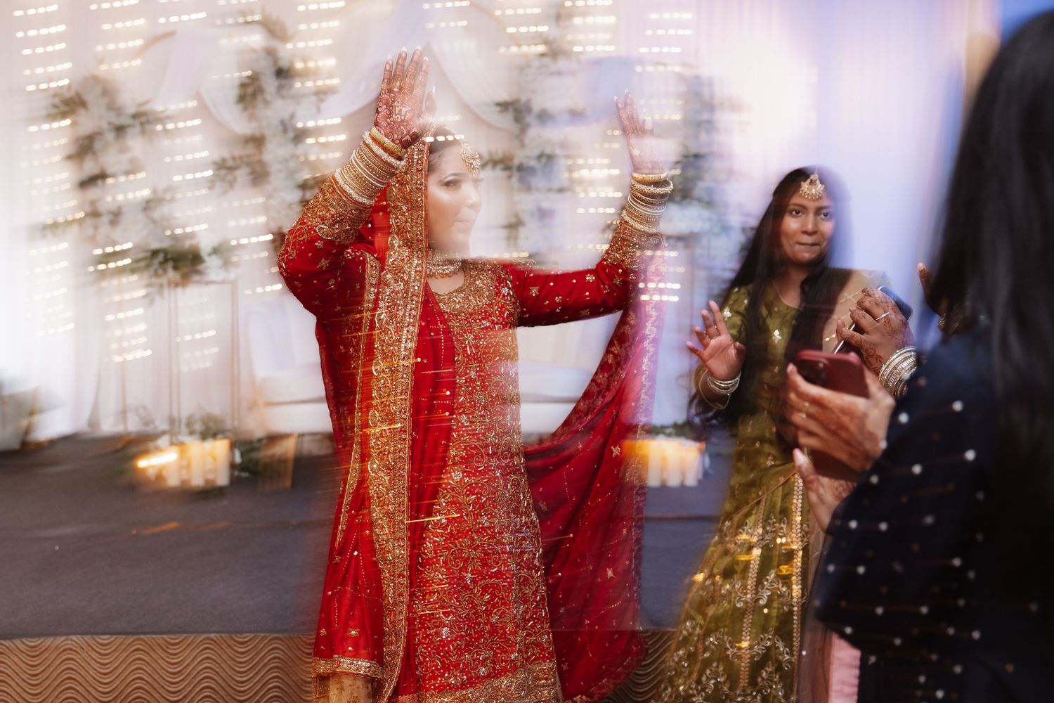 Bride in red traditional Indian wedding attire dancing gracefully with hands raised at celebration.