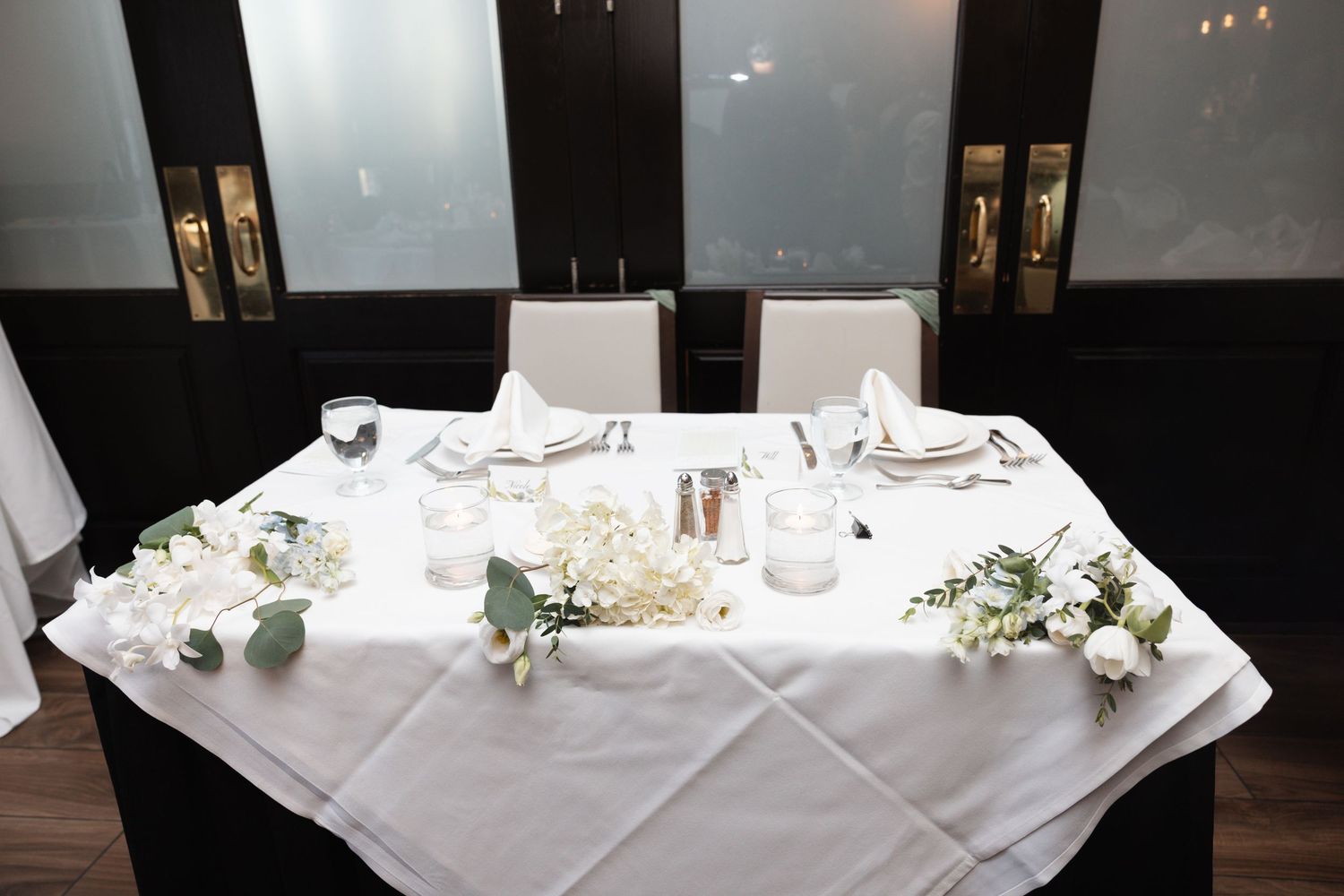 Elegant wedding sweetheart table set with white linens, floral arrangements, and candles for reception.