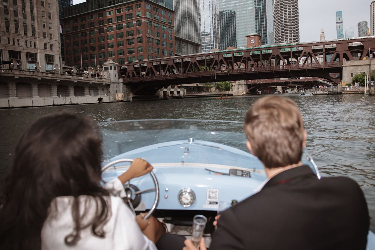 Couple cruising down the Chicago River on a classic vintage blue boat under an iron bridge.