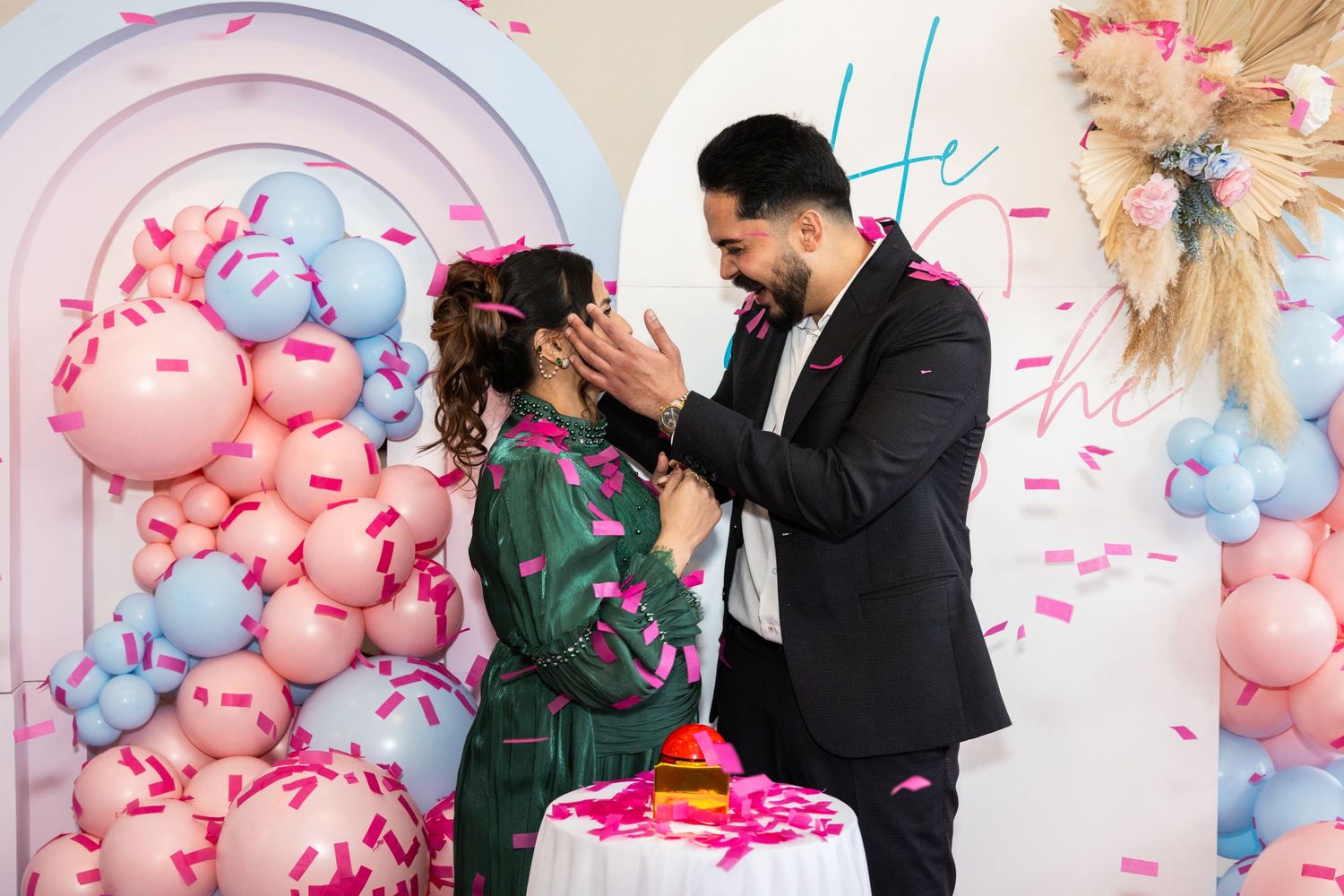 Couple laughing together at gender reveal party surrounded by pink confetti and balloons.