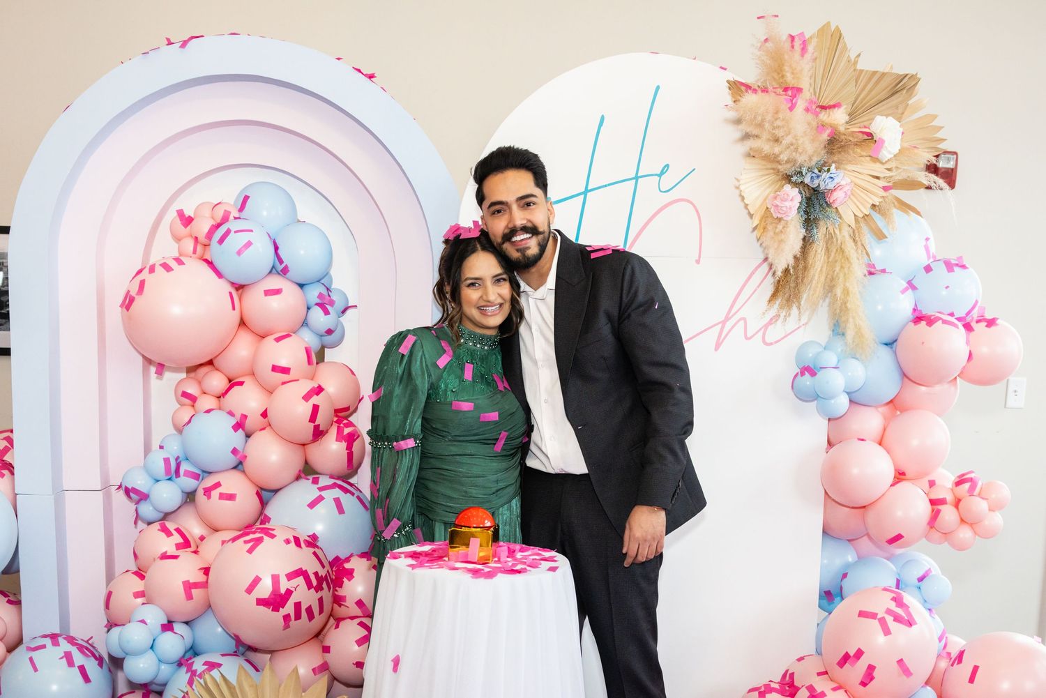 Happy couple embracing at gender reveal party with pink and blue balloon decorations.