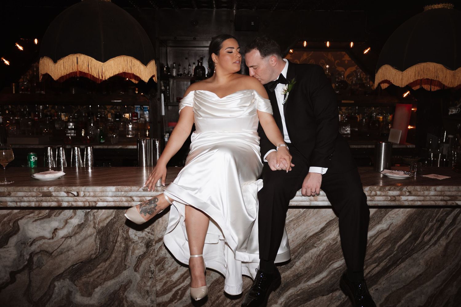 Bride and groom sit together at marble bar during wedding reception.