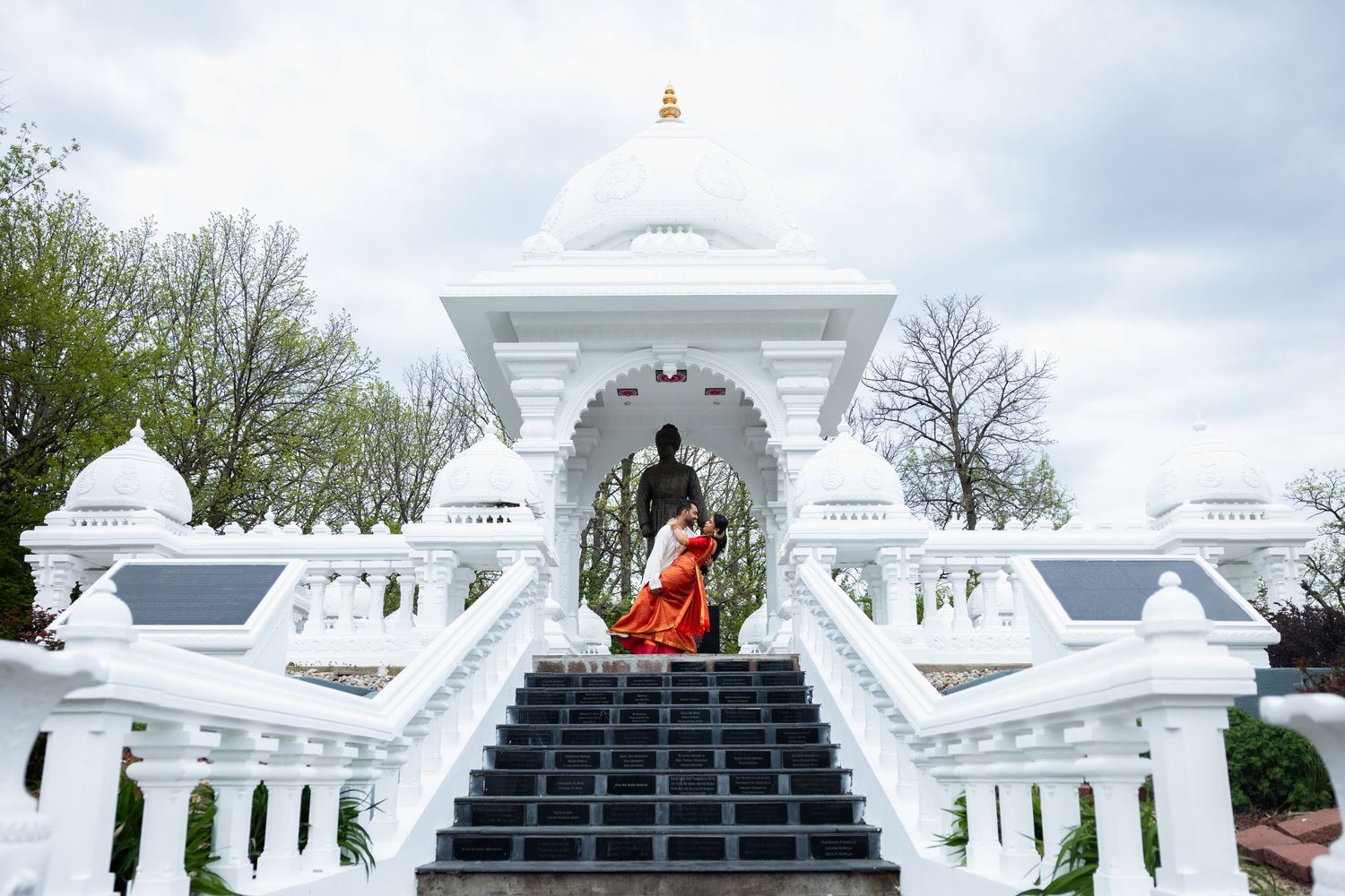 Bride in red saree ascending steps of a white Hindu temple during wedding ceremony.