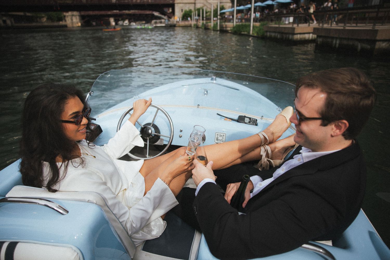 Couple clinking champagne glasses on a light blue speedboat on the Chicago River, enjoying a romantic boat ride.