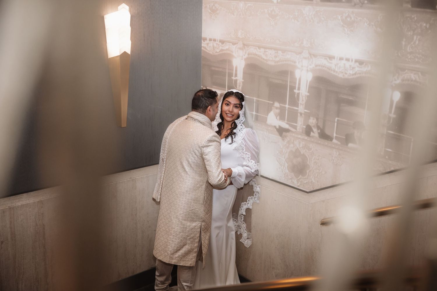 Couple sharing intimate first look moment on staircase in softly lit elegant wedding venue.