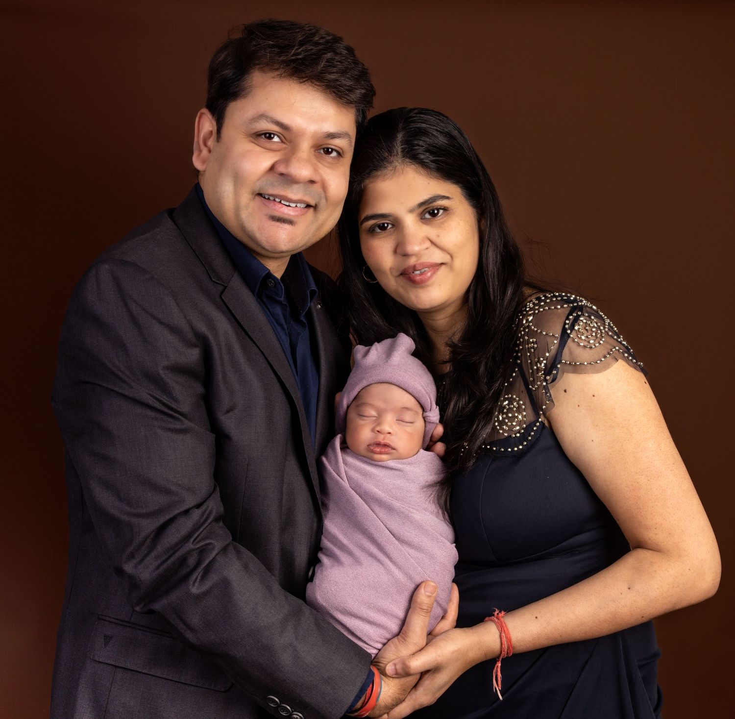 Happy Indian couple posing with their newborn baby wrapped in purple for a family portrait photo.