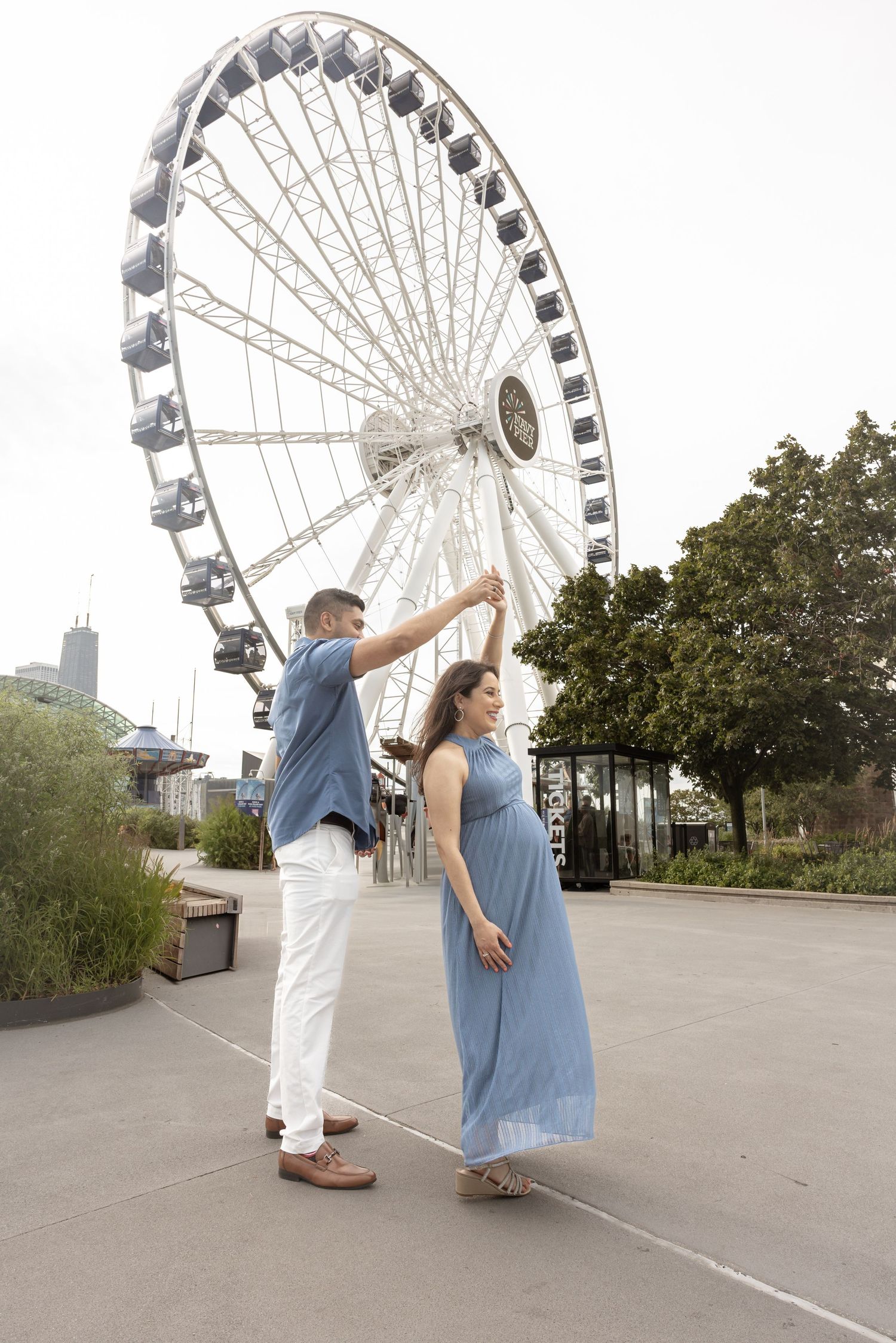 Couple sharing a romantic dance outdoors near a white Ferris wheel, woman in flowing blue dress being spun gracefully.