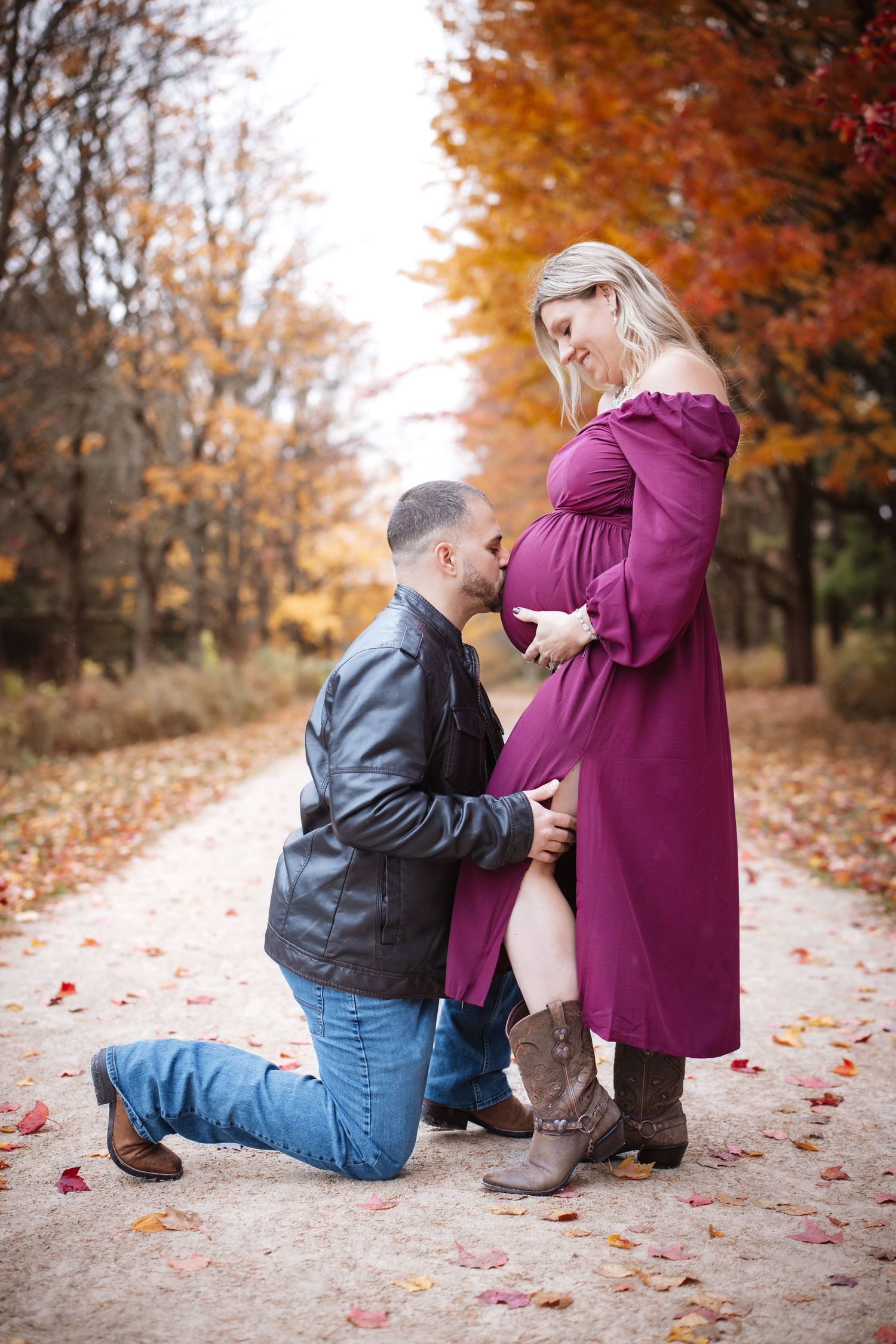 Man kneeling kissing pregnant womans belly in autumn park setting.