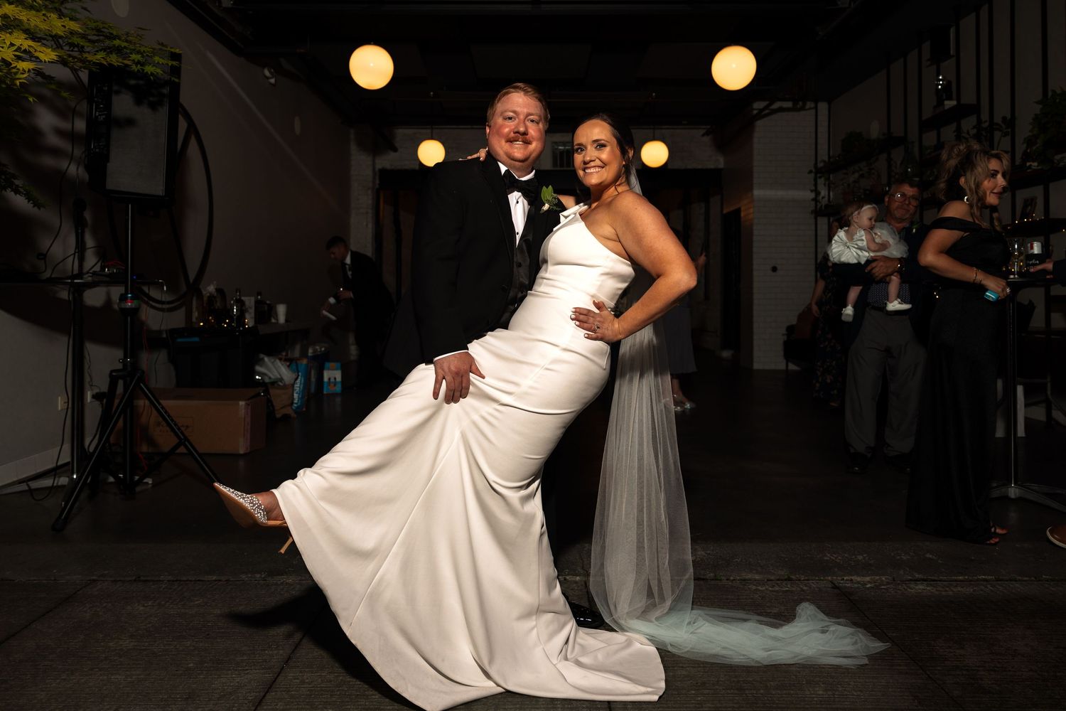 Groom lifting bride's leg in a playful pose at their wedding reception venue.