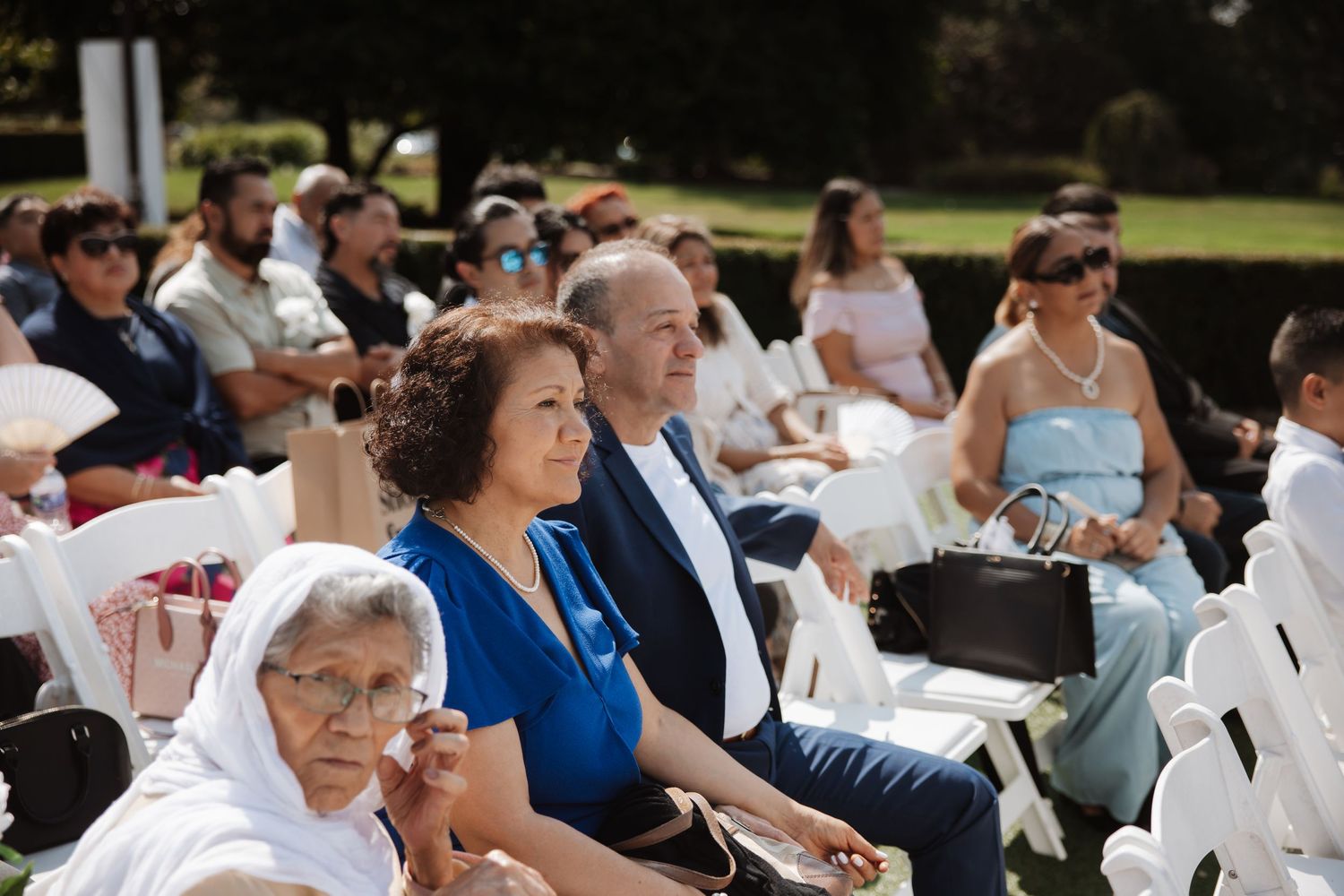 Wedding guests including woman in blue dress seated at elegant outdoor wedding ceremony.