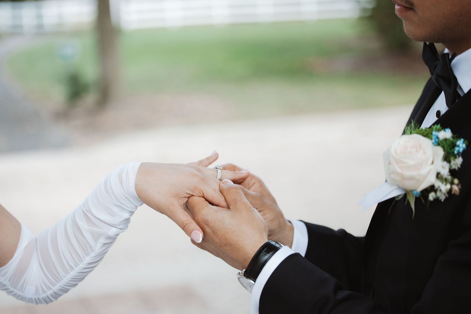 Bride placing a wedding ring on groom's finger during outdoor ceremony, close-up of hands.