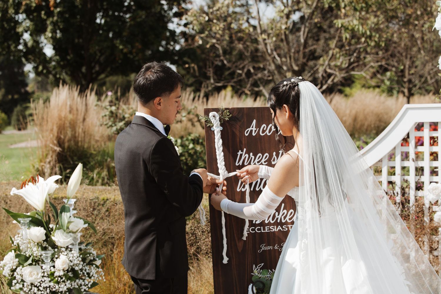 Bride and groom perform cord of three strands unity ceremony at outdoor wedding altar.