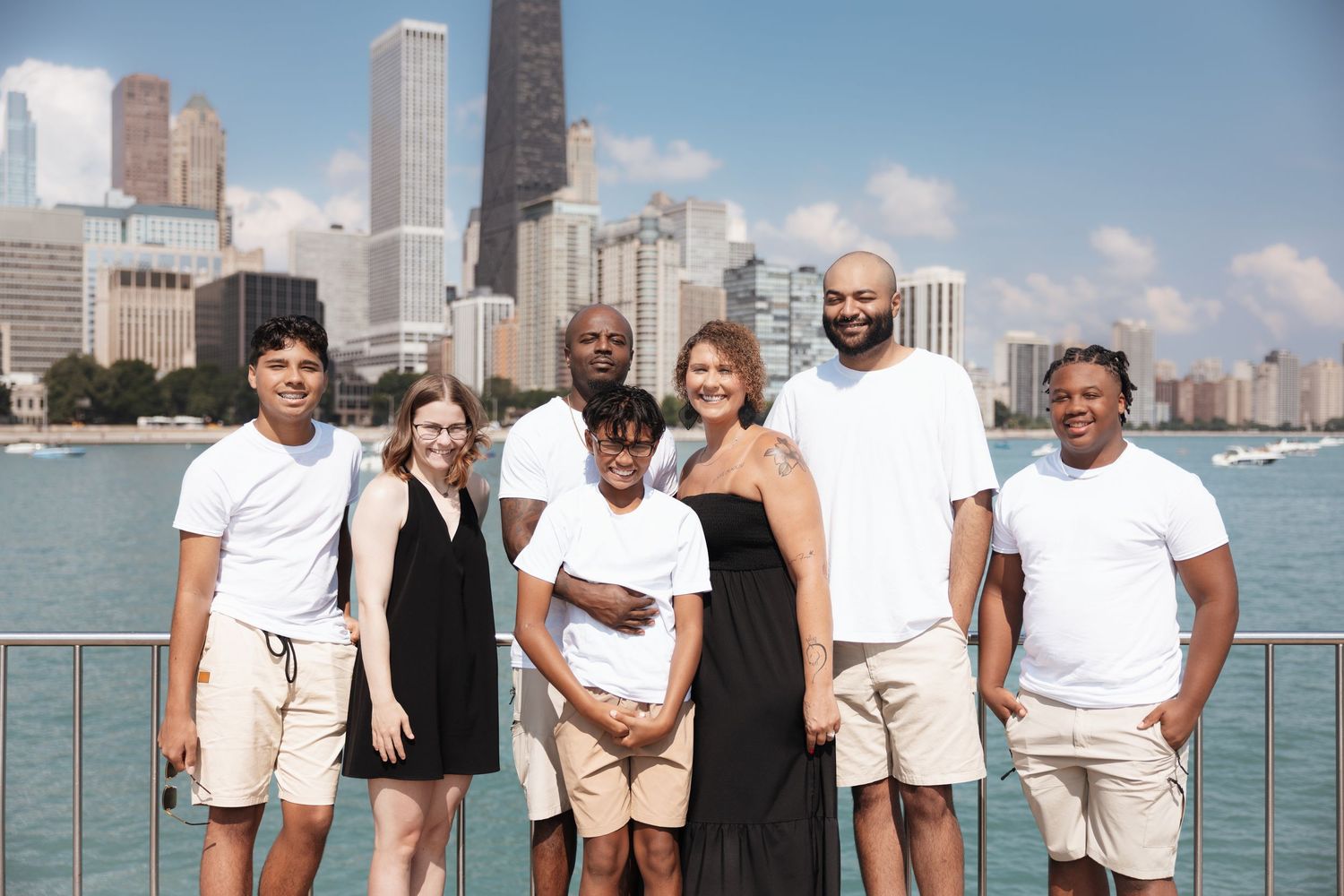 Group of seven people smiling together outdoors with Chicago skyline and Lake Michigan in the sunny background.