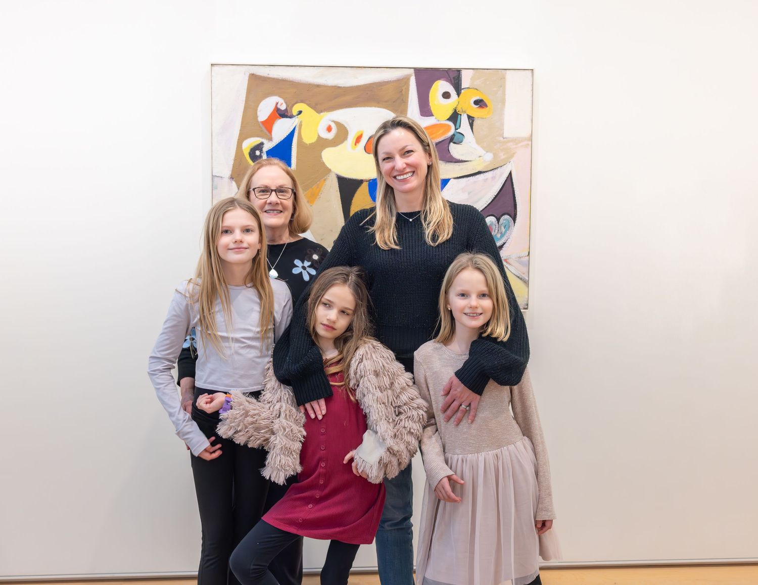 Group of women and girls posing happily before a vibrant abstract painting in a gallery.