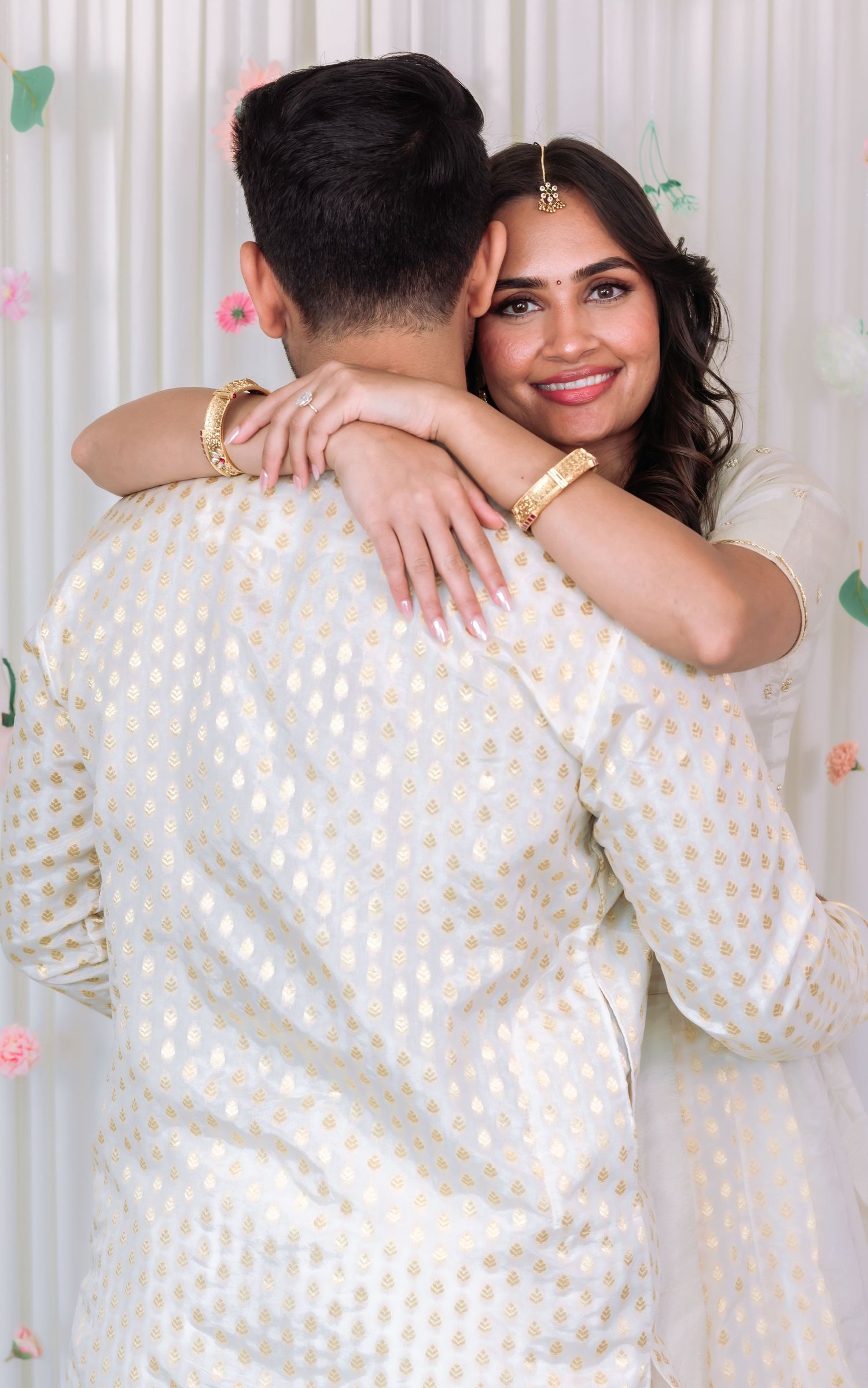 Bride in white and gold lehenga shares a joyful embrace with groom during Indian wedding celebration.