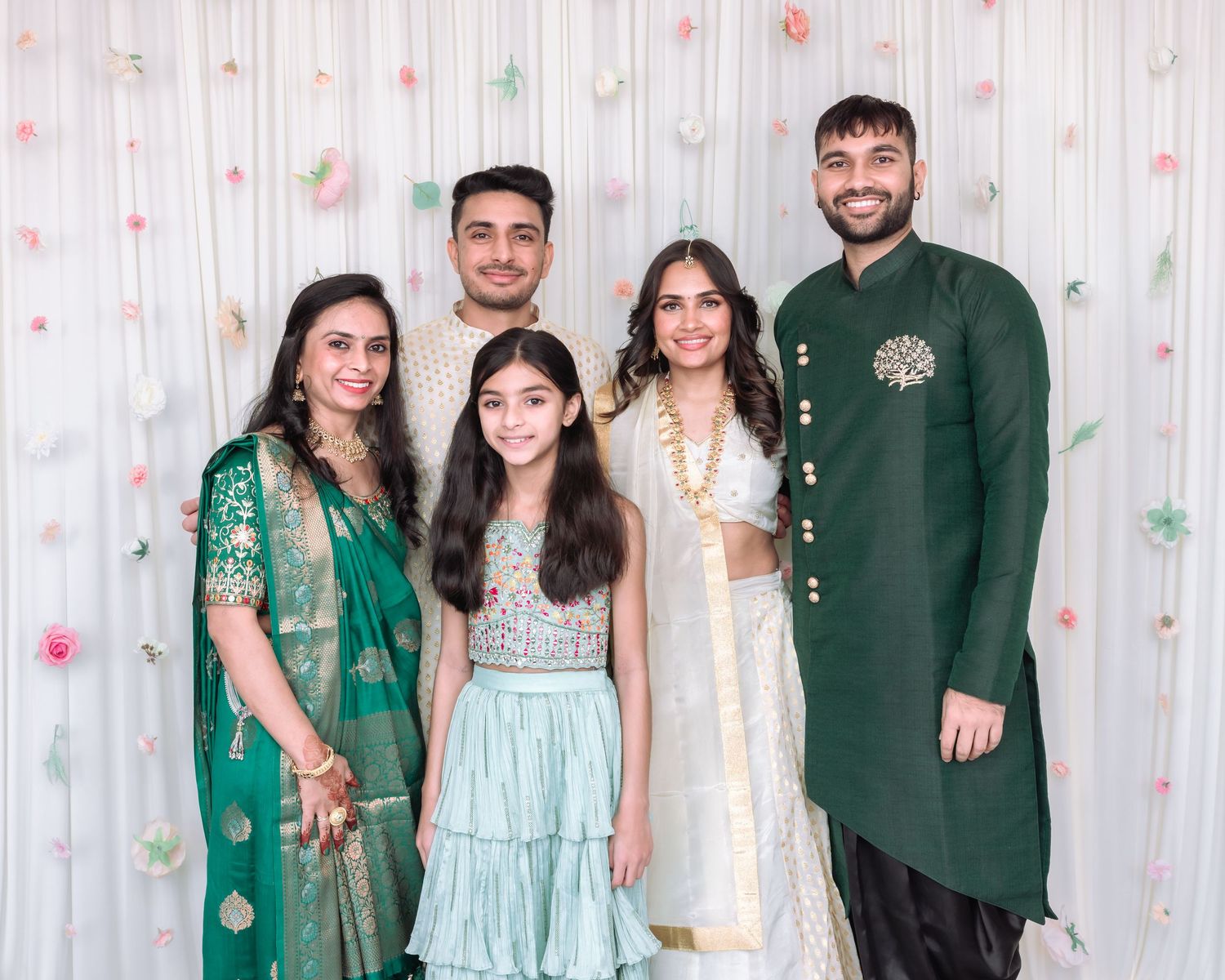 Indian family of five posing in traditional green and white wedding attire at a celebration.