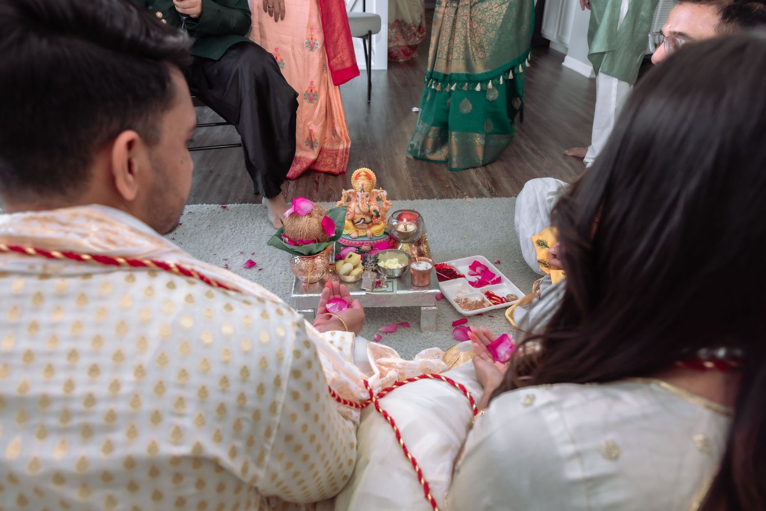 Indian wedding couple performing Ganesh puja ritual with sacred items and red thread during Hindu ceremony.